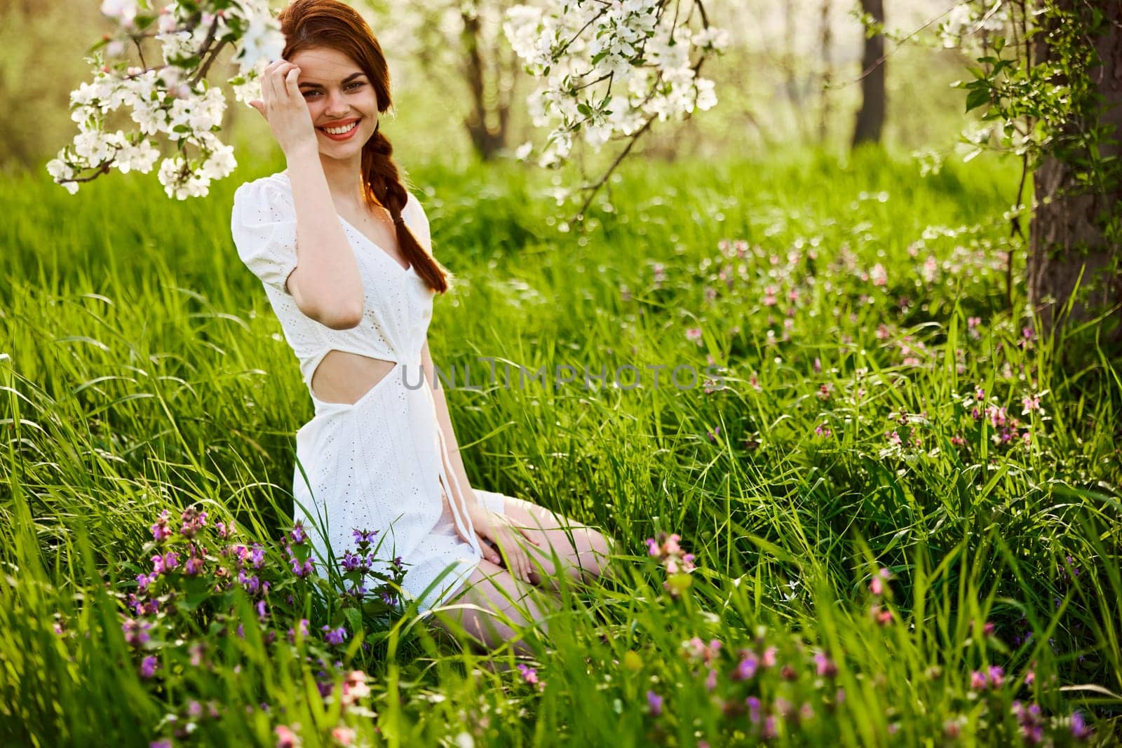 a young woman in a light summer dress is resting sitting under a flowering tree. High quality photo