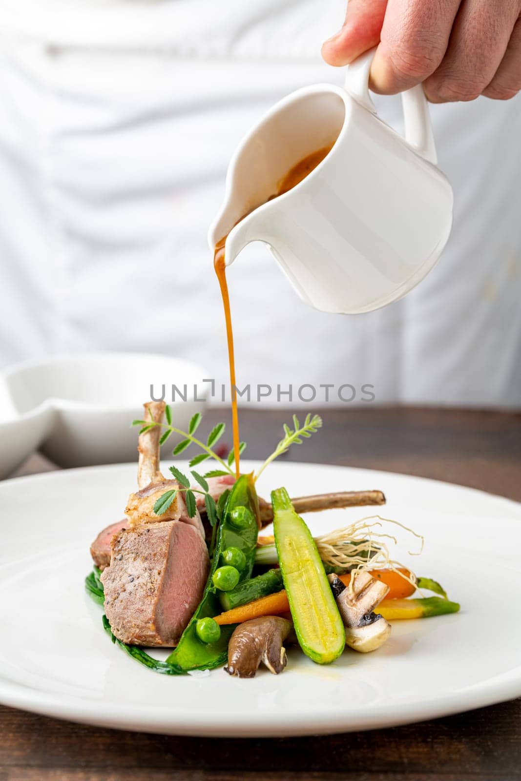 Chef pouring sauce on lamb chops with various vegetables at a fine dining restaurant