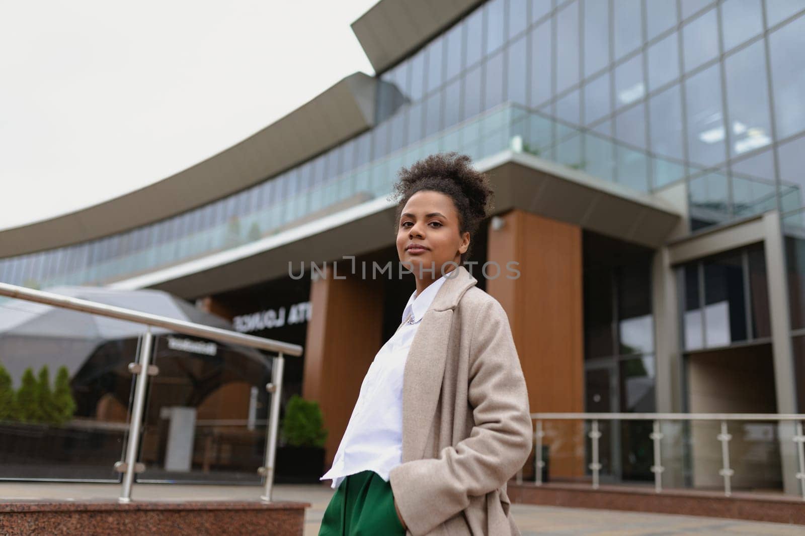 American young woman designer stands thoughtfully in front of a glass business center.