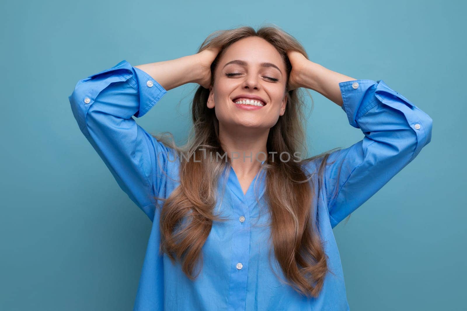 close-up of a lucky cute stylish blond girl in a blue shirt grimacing on a blue bright isolated background.