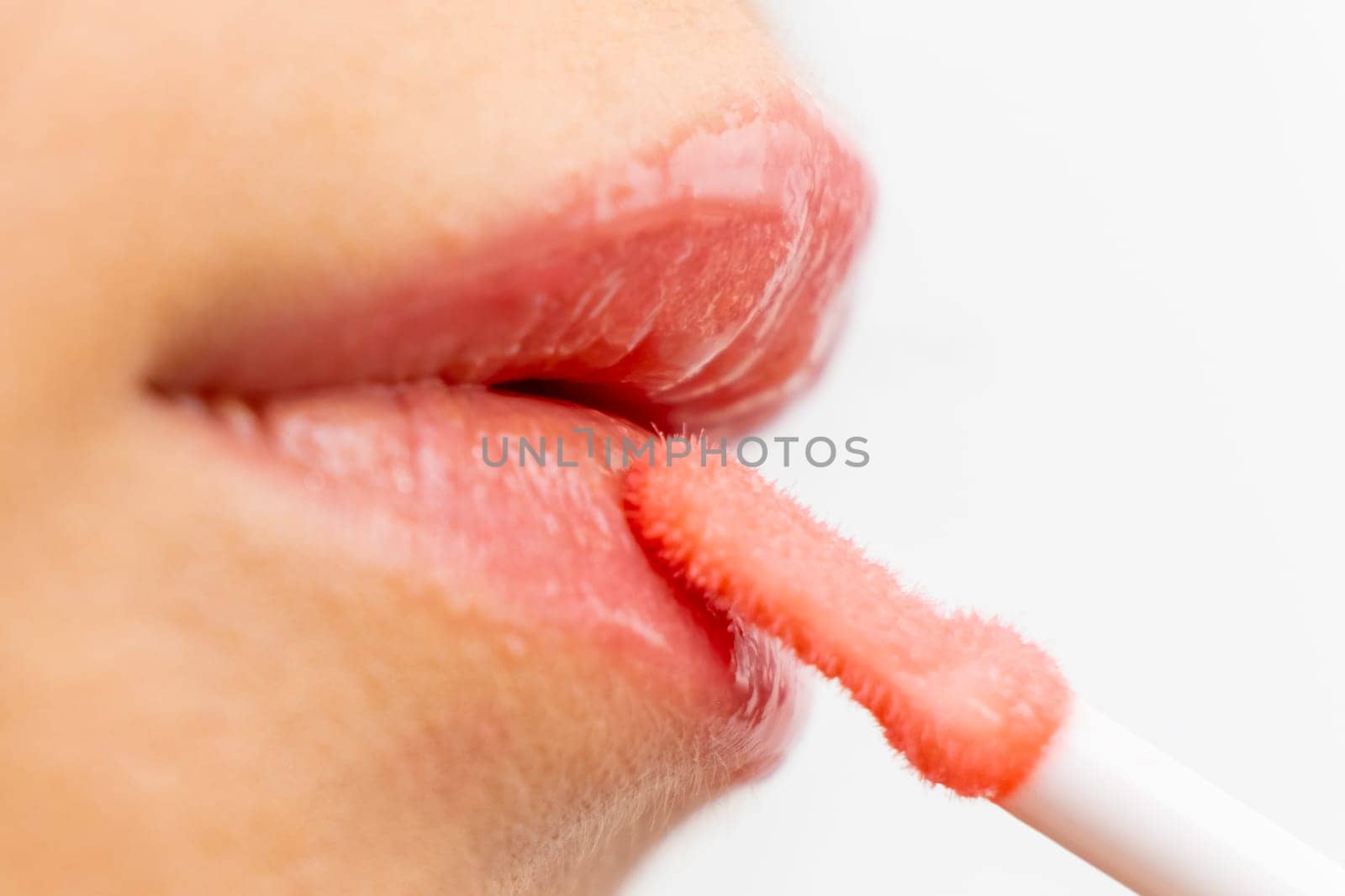 Makeup artist applying lip gloss on the white background.