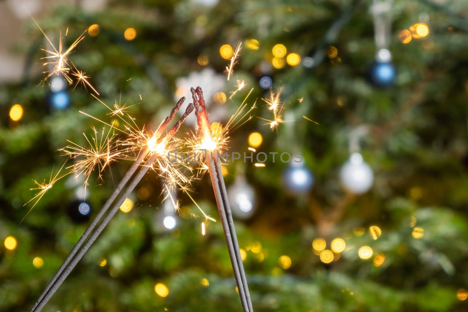 Two sparklers on the background of the Christmas tree. A couple celebrating New Year holding Bengal lights