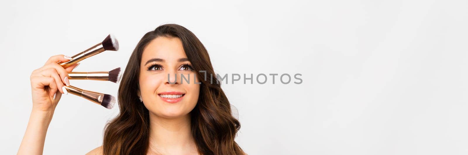Charming woman holding golden makeup brushes and smiling.