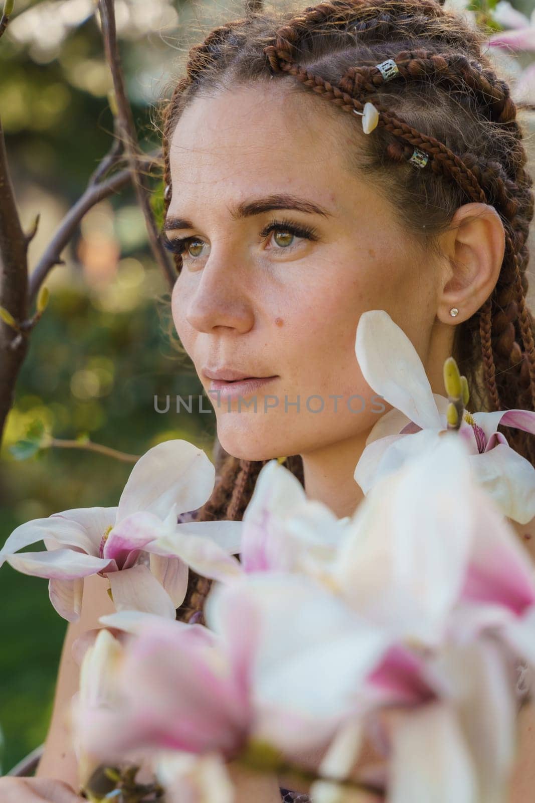 Magnolia flowers. Happy woman enjoys by blooming magnolia tree and sniffs it flowers with closed eyes in spring garden. Portrait