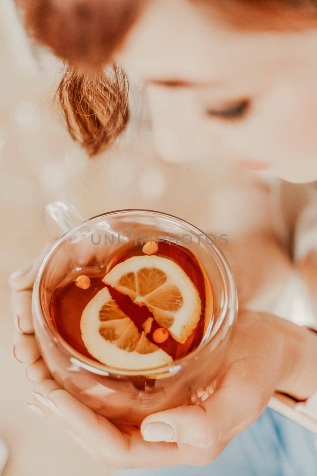 Cup of tea with lemon in female hands. Top view of female hands holding a transparent cup of tea with lemon