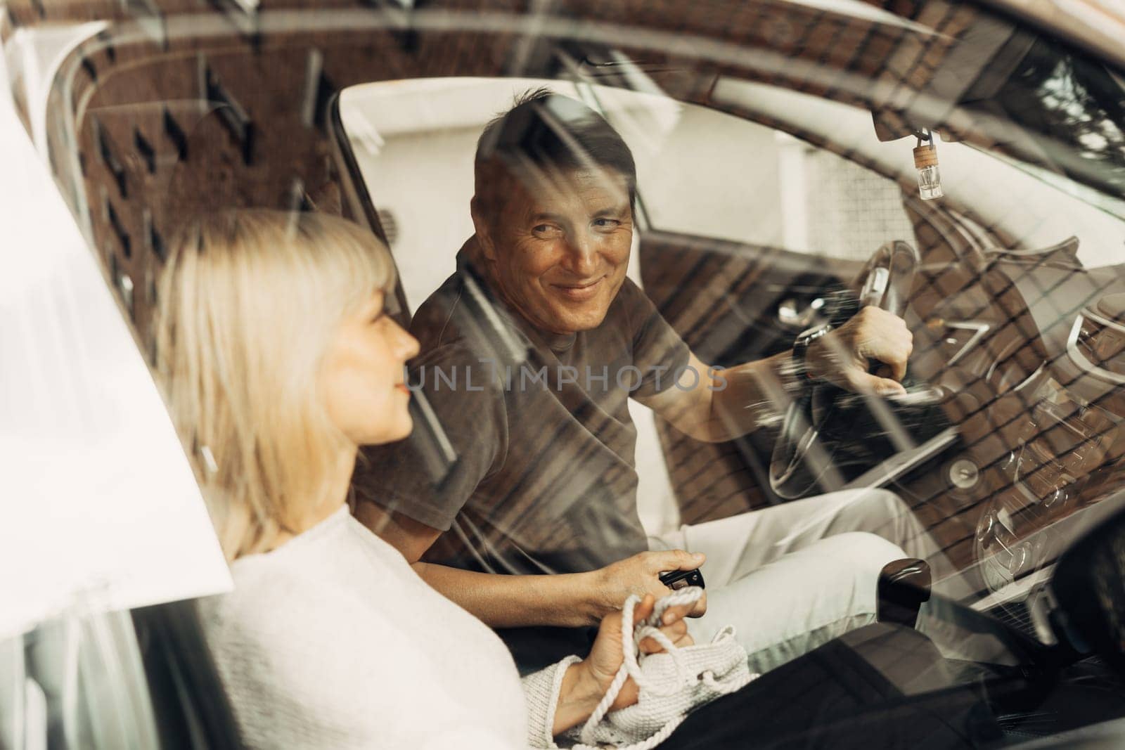 An adult mature happy romantic couple in love outdoors in car. A blonde caucasian man and woman spend time together. Senior wife and husband sit in the car to go for a walk