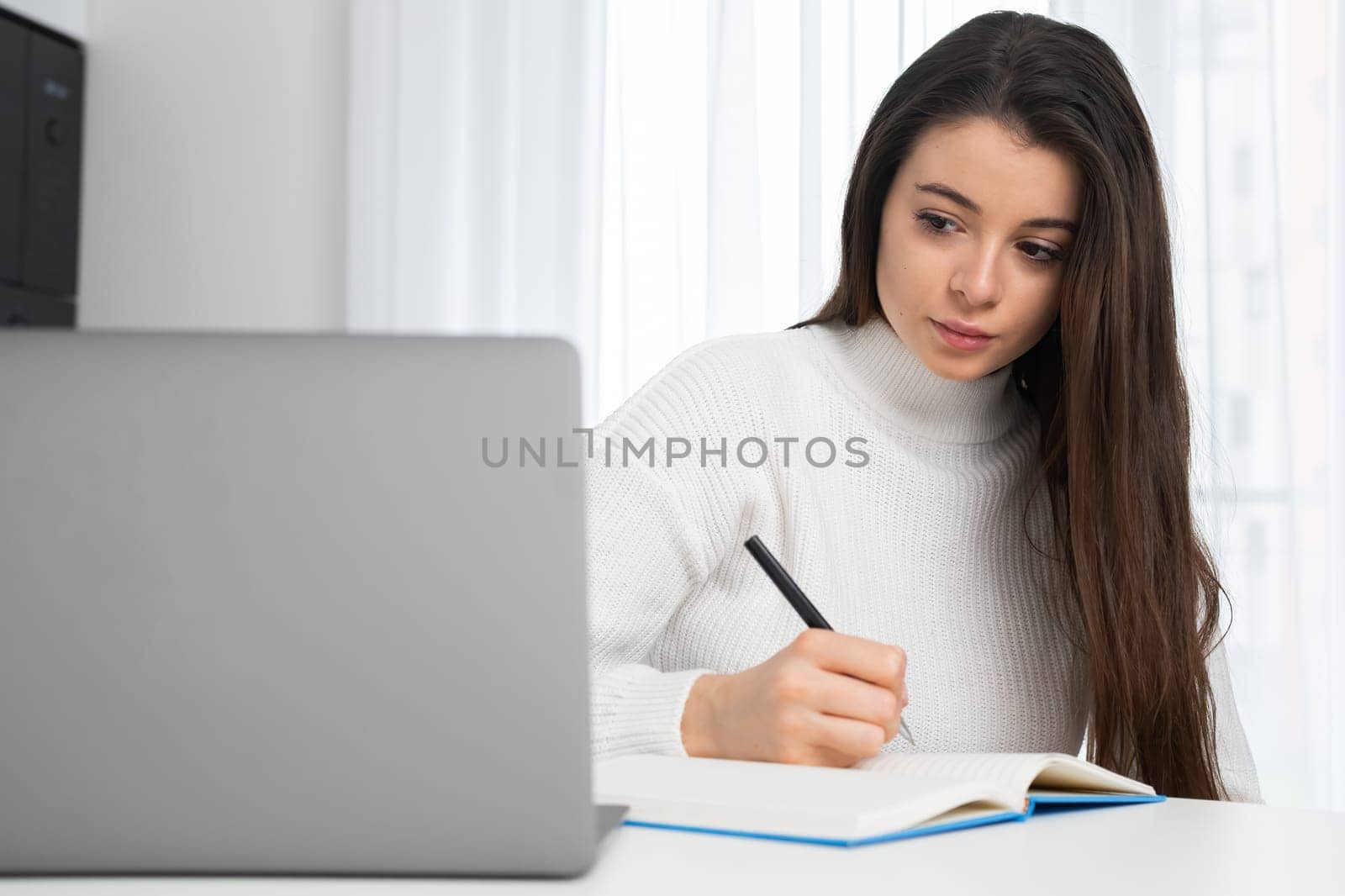 Serious young lady in stylish wear attends online lecture and makes notes with copy space.