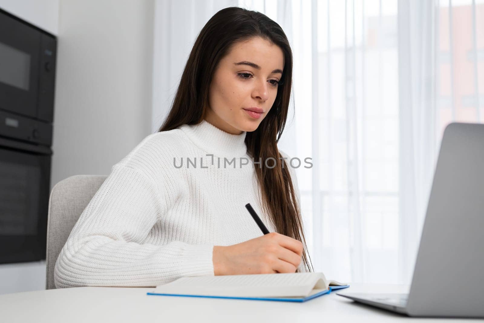 Modern female student in casual clothes studying remotely using laptop. Online education at home concept.