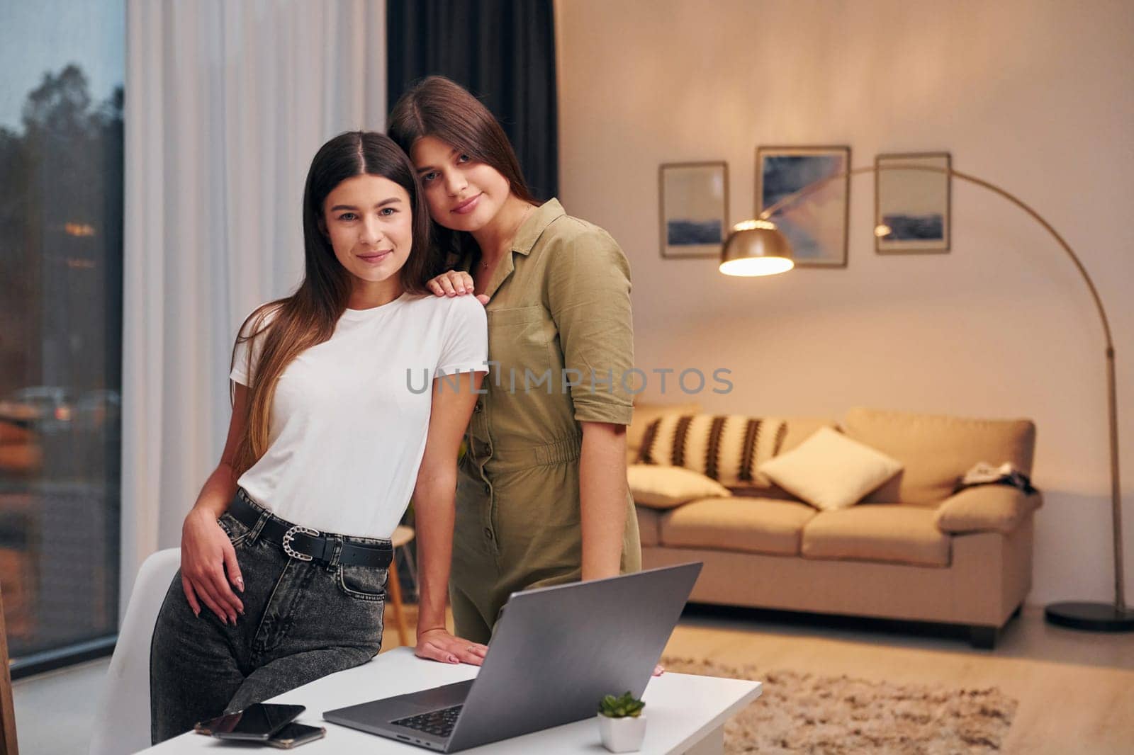 Two women in casual clothes is standing indoors at home.