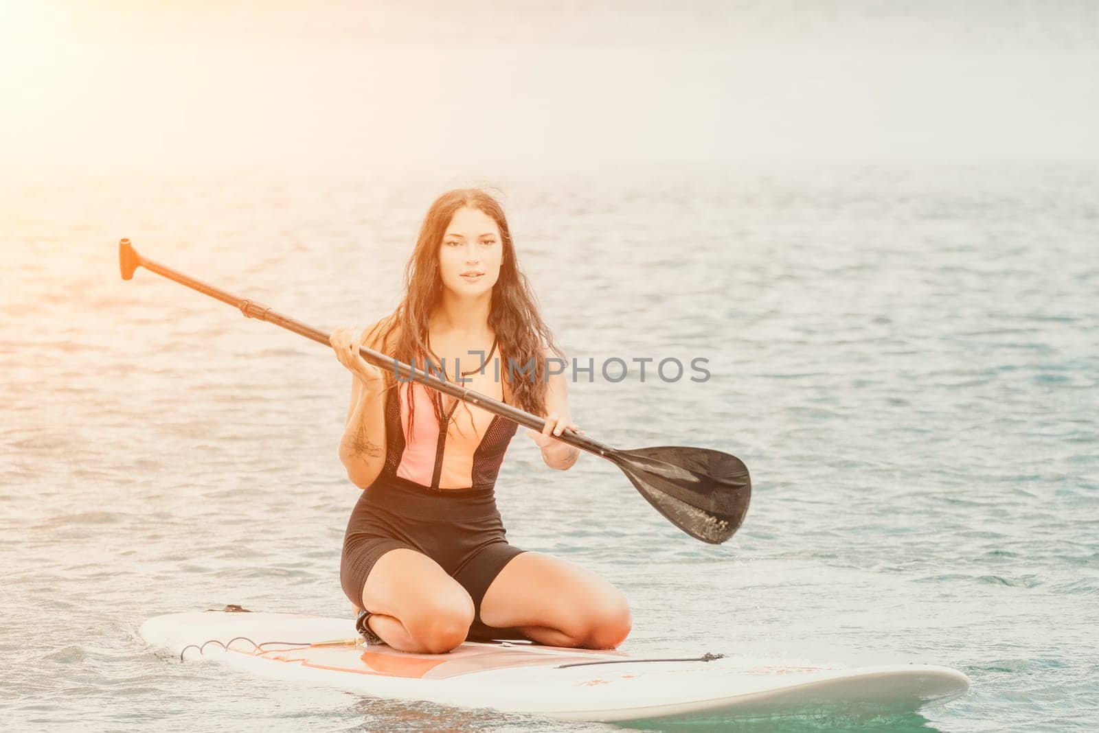 Close up shot of beautiful young caucasian woman with black hair and freckles looking at camera and smiling. Cute woman portrait in a pink bikini posing on sup board in the sea by panophotograph