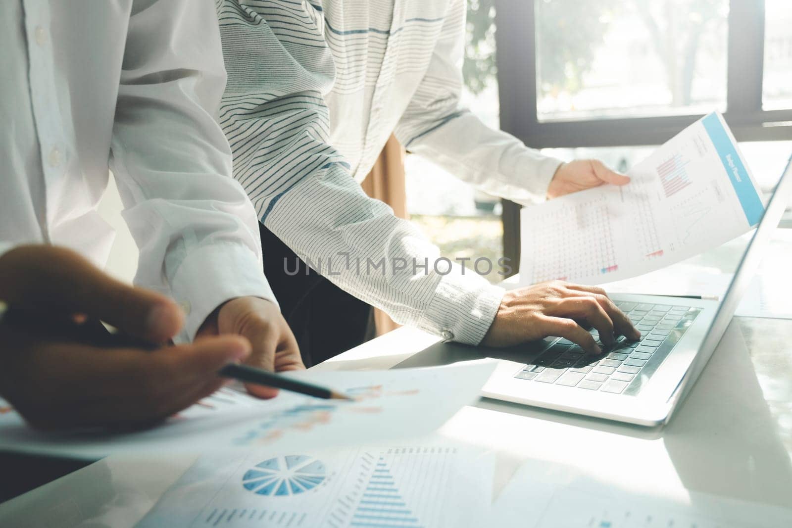 Close-up of businessmen working, meeting together at desk in workplace, office using laptop, holding pencils and pointing at graph documents for discussing about strategies, plans, analytic progress, and financial stats of company. Business, Teamwork concept.