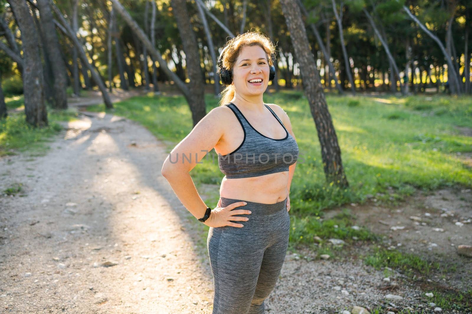 Fat woman and sports. Girl doing exercise for weight loss in the fresh air and laughing in camera after training. Copy space and empty space for text or advertising by Satura86