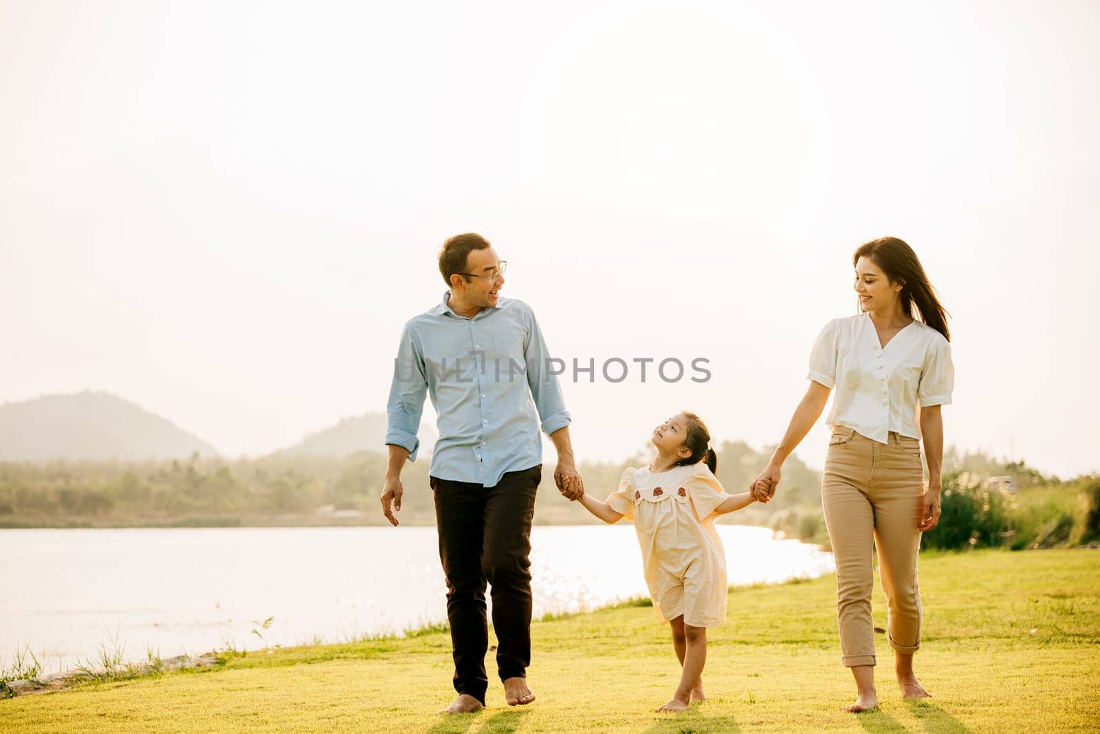 Asian family and daughter running and holding hands in a beautiful park, with a sunny sky and a feeling of love and happiness, Happy Family Day Concept