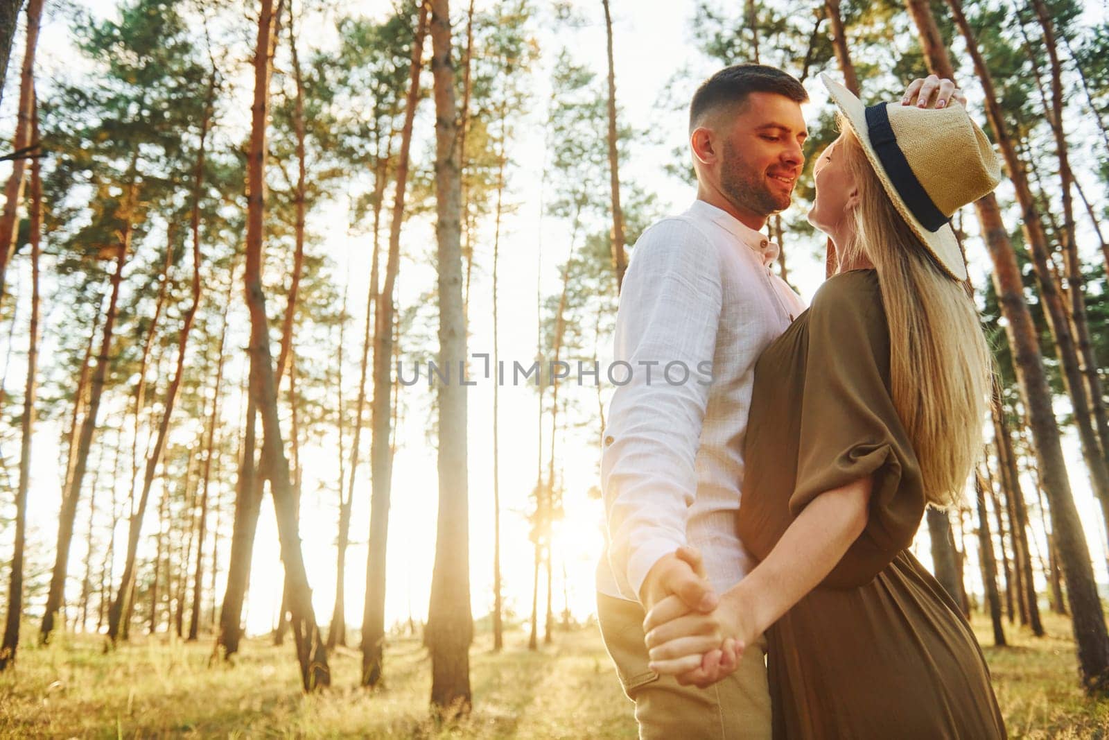 Holding each other by the hands. Happy couple is outdoors in the forest at daytime.