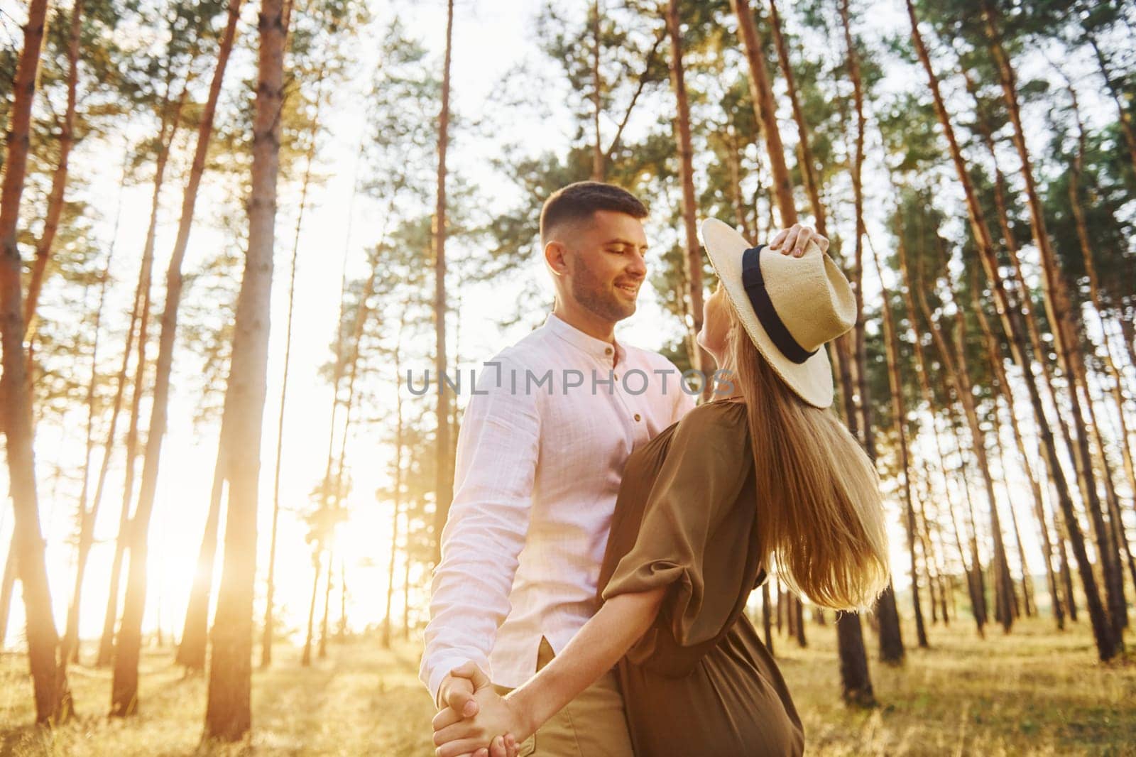 Holding each other by the hands. Happy couple is outdoors in the forest at daytime.