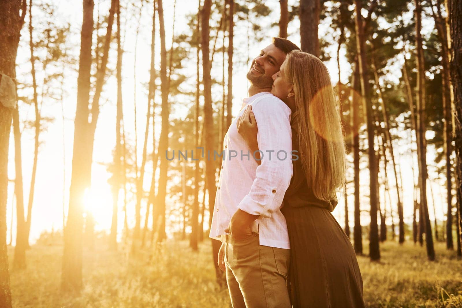 Illuminated by sunlight. Happy couple is outdoors in the forest at daytime.