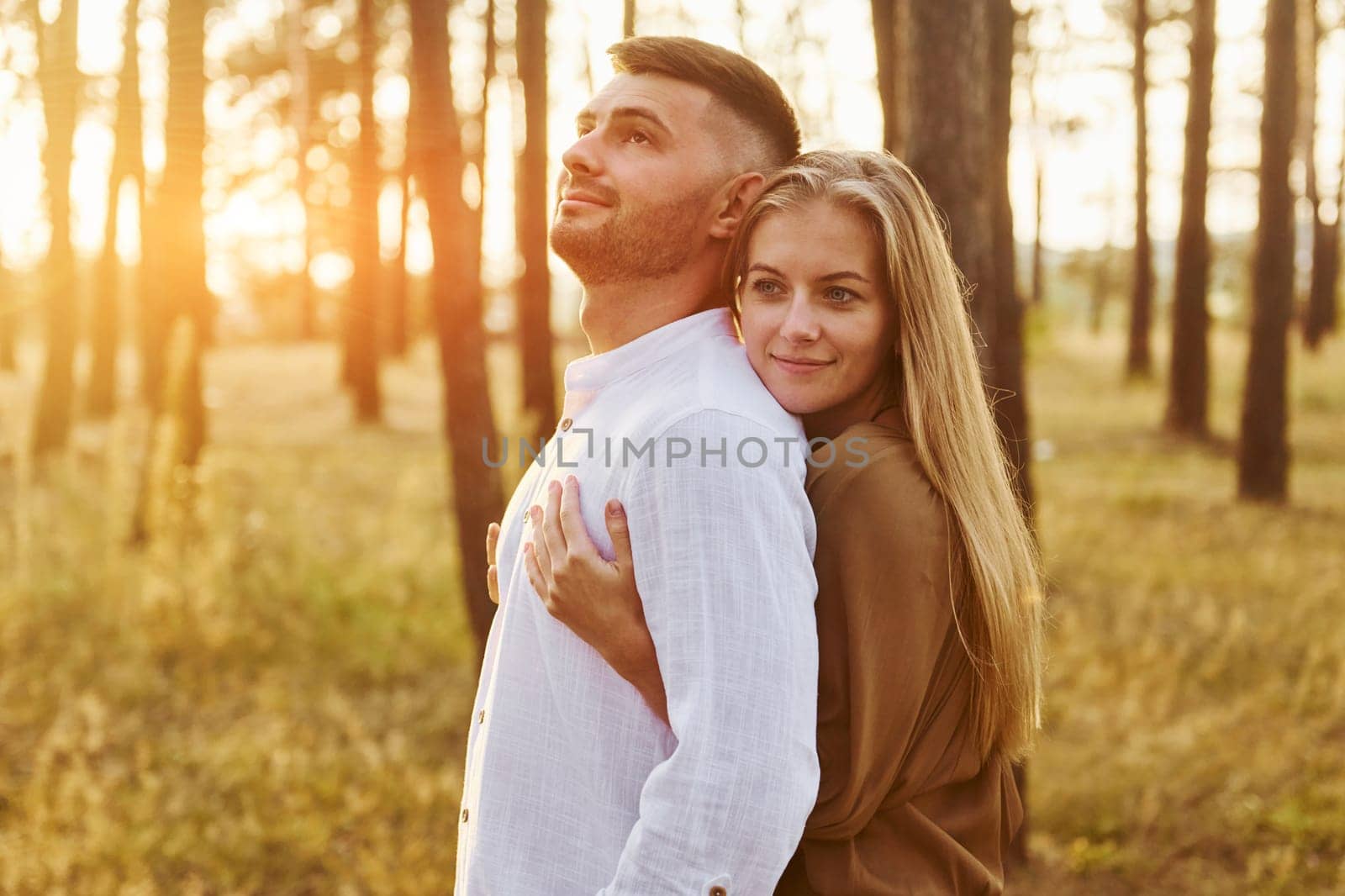 Illuminated by sunlight. Happy couple is outdoors in the forest at daytime.