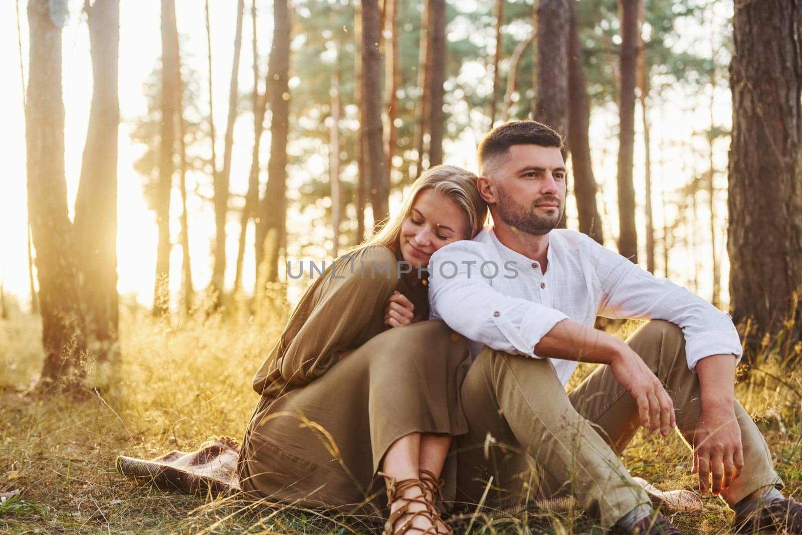 Illuminated by sunlight. Happy couple is outdoors in the forest at daytime.