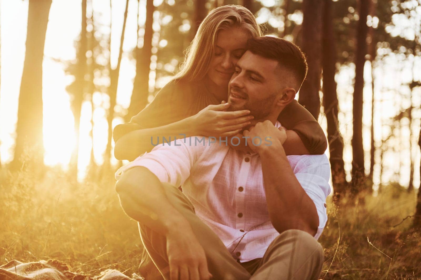 Sitting on the ground. Happy couple is outdoors in the forest at daytime.