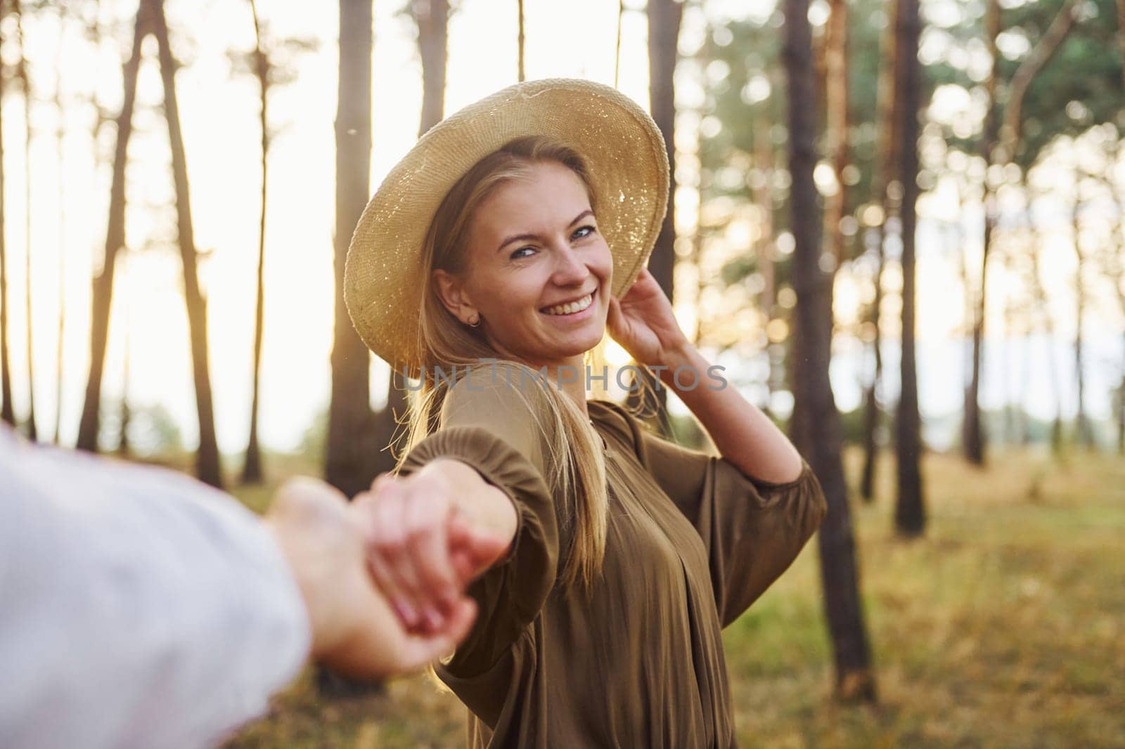 Woman holding man's hand. Happy couple is outdoors in the forest at daytime.