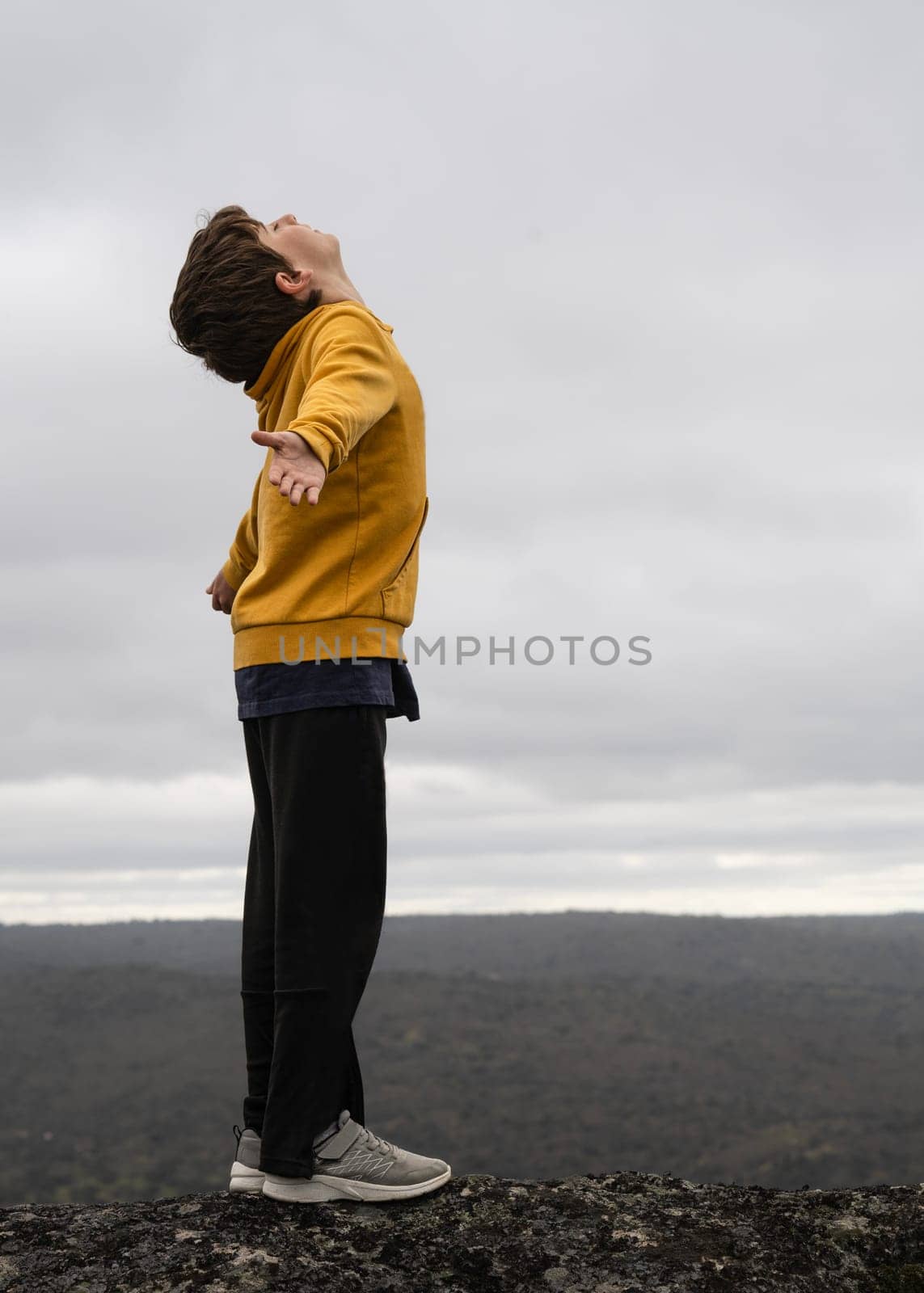 Side view portrait of a young kid breathing fresh air in the top of a mountain.