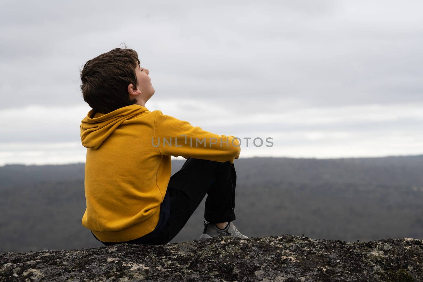side view Portrait of a young kid breathing fresh air sitting in the top of a mountain with closed eyes by papatonic