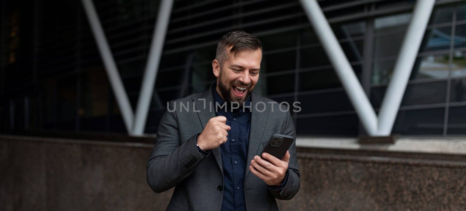 happy freelancer man with a smartphone in his hands smiling against the backdrop of the building.