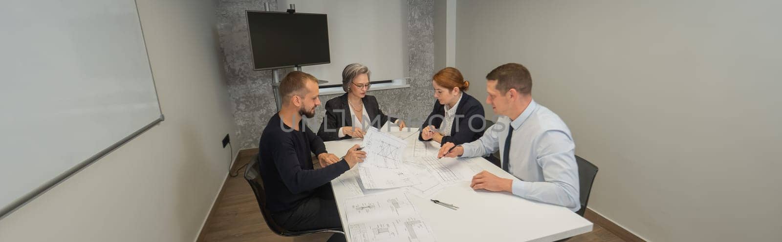 Four business people sitting around a table discussing blueprints. Designers engineers at a meeting. Widescreen