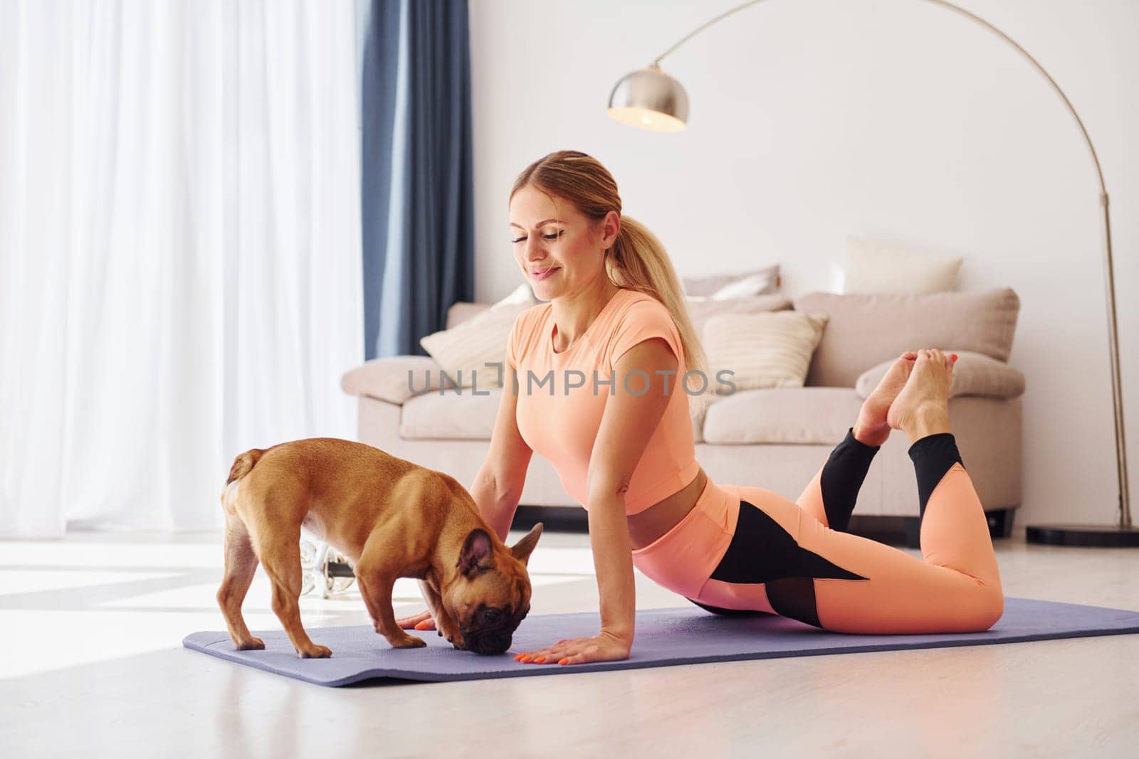Woman in yoga clothes with pug dog is at home at daytime.