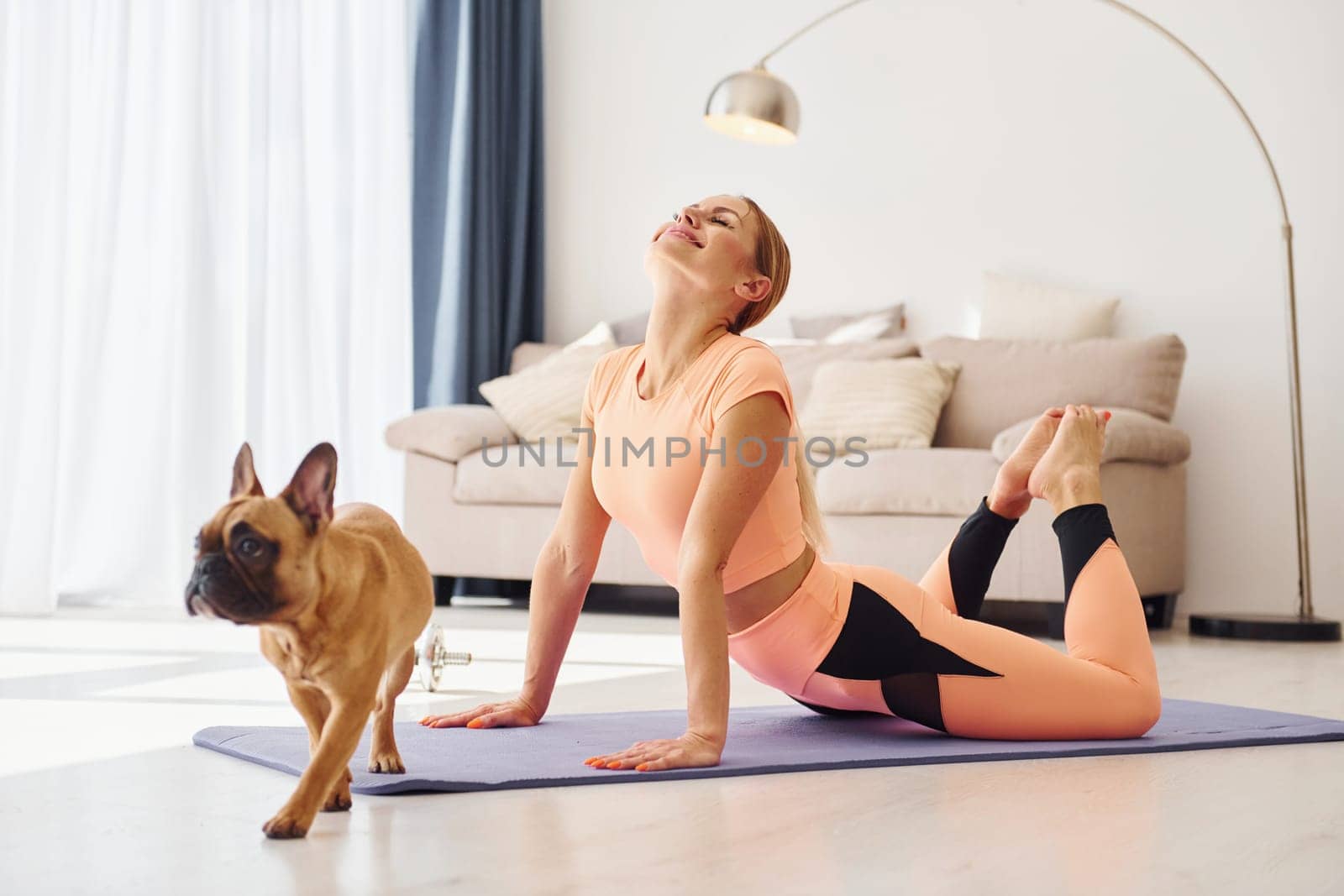 Woman in yoga clothes with pug dog is at home at daytime.