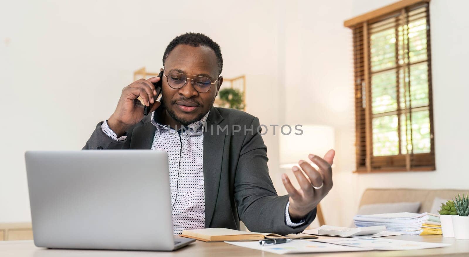 Portrait of handsome African black young business man working on laptop and talking phone at office desk...