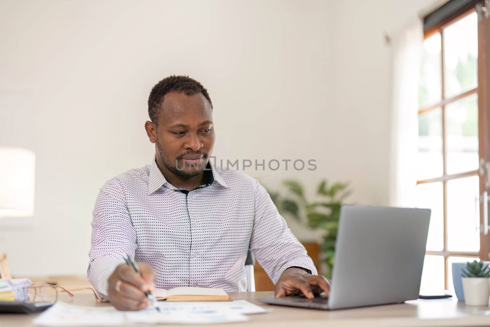 Portrait of handsome African black young business man working on laptop at office desk...