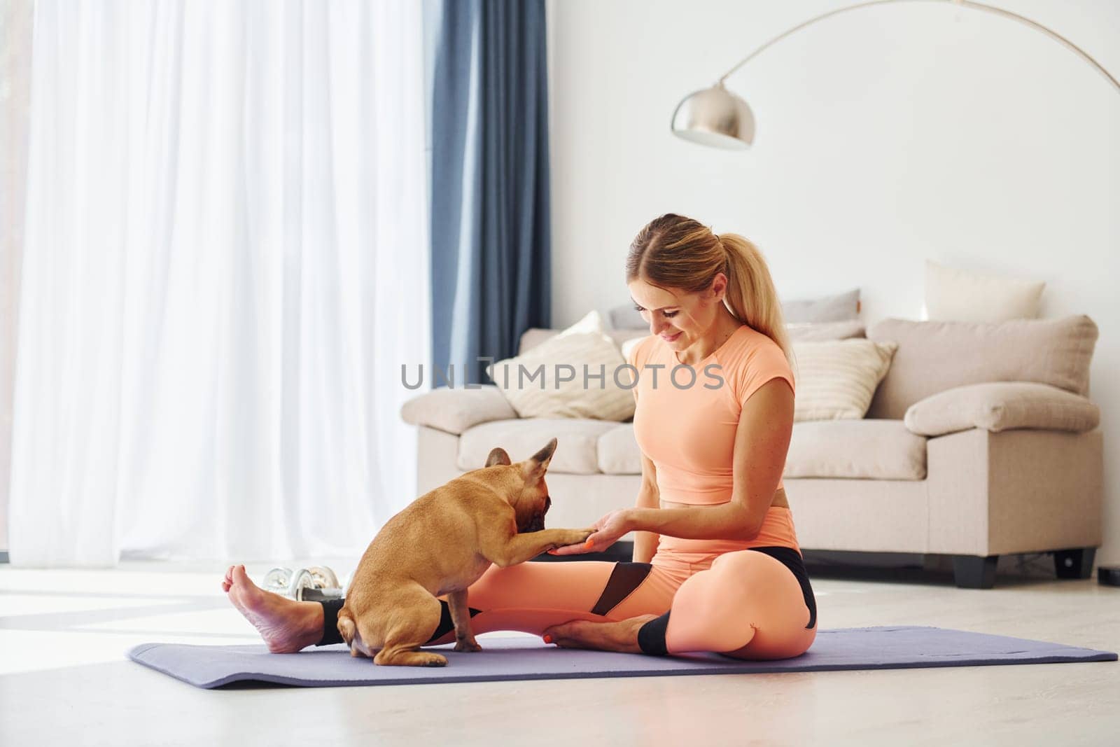 On fitness mat. Woman with pug dog is at home at daytime.