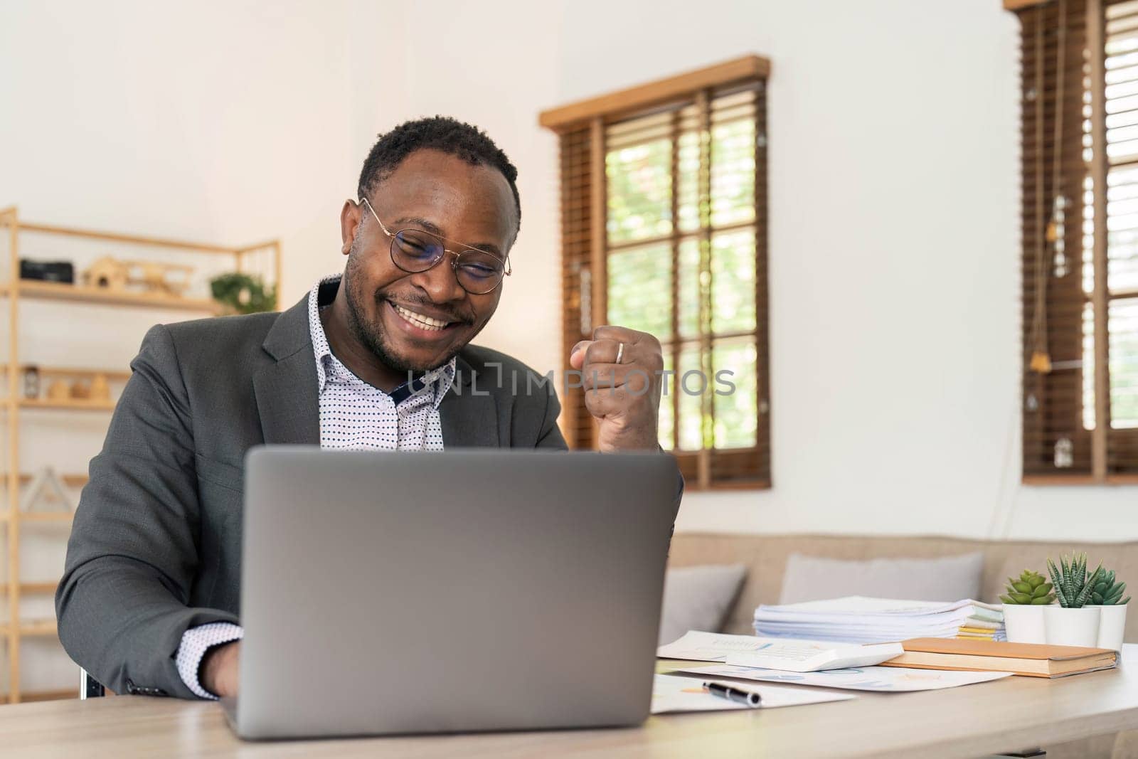 Success at work, good deal. African-American guy looks at the laptop screen, screams excitedly and raises his fists in a victory gesture at home...