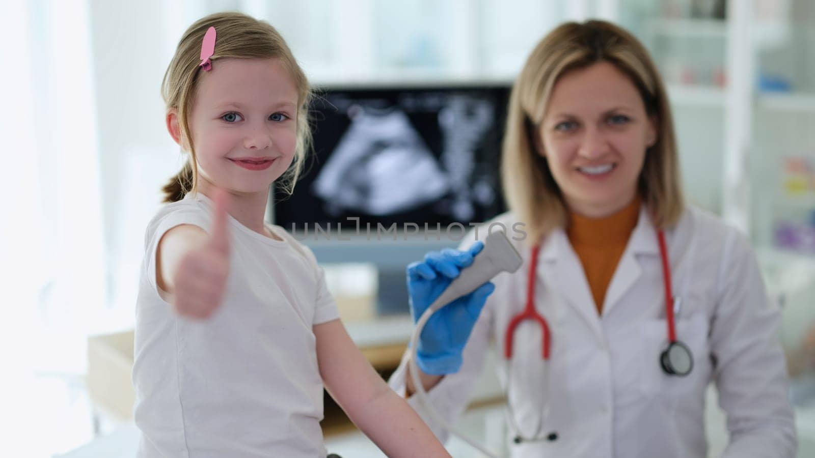 Little girl showing thumbs up at doctor appointment with ultrasound diagnostics in clinic. High quality professional instrumental medical examination in children concept