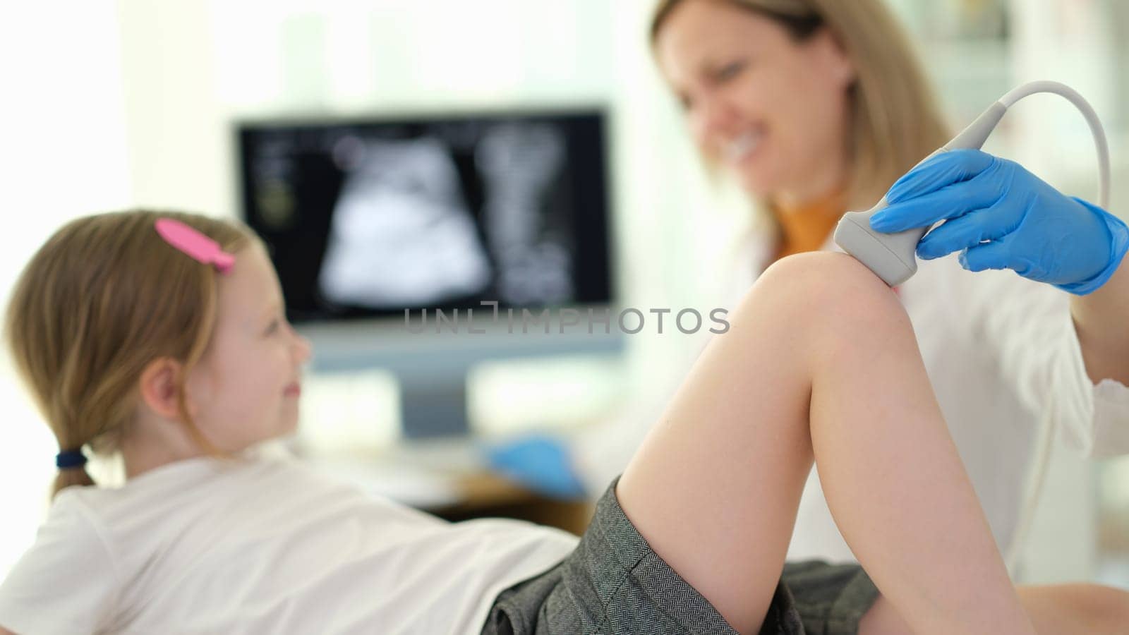 Doctor pediatrician conducting ultrasound examination of knee joint of child in clinic closeup. Diagnosis of rheumatic diseases in children concept