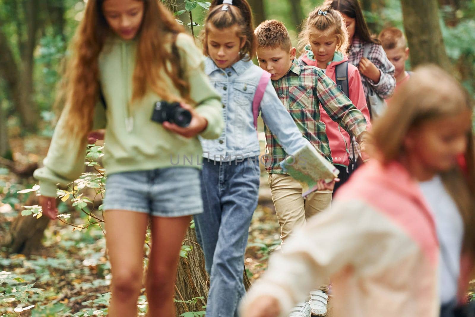 With touristic equipment. Kids in green forest at summer daytime together.