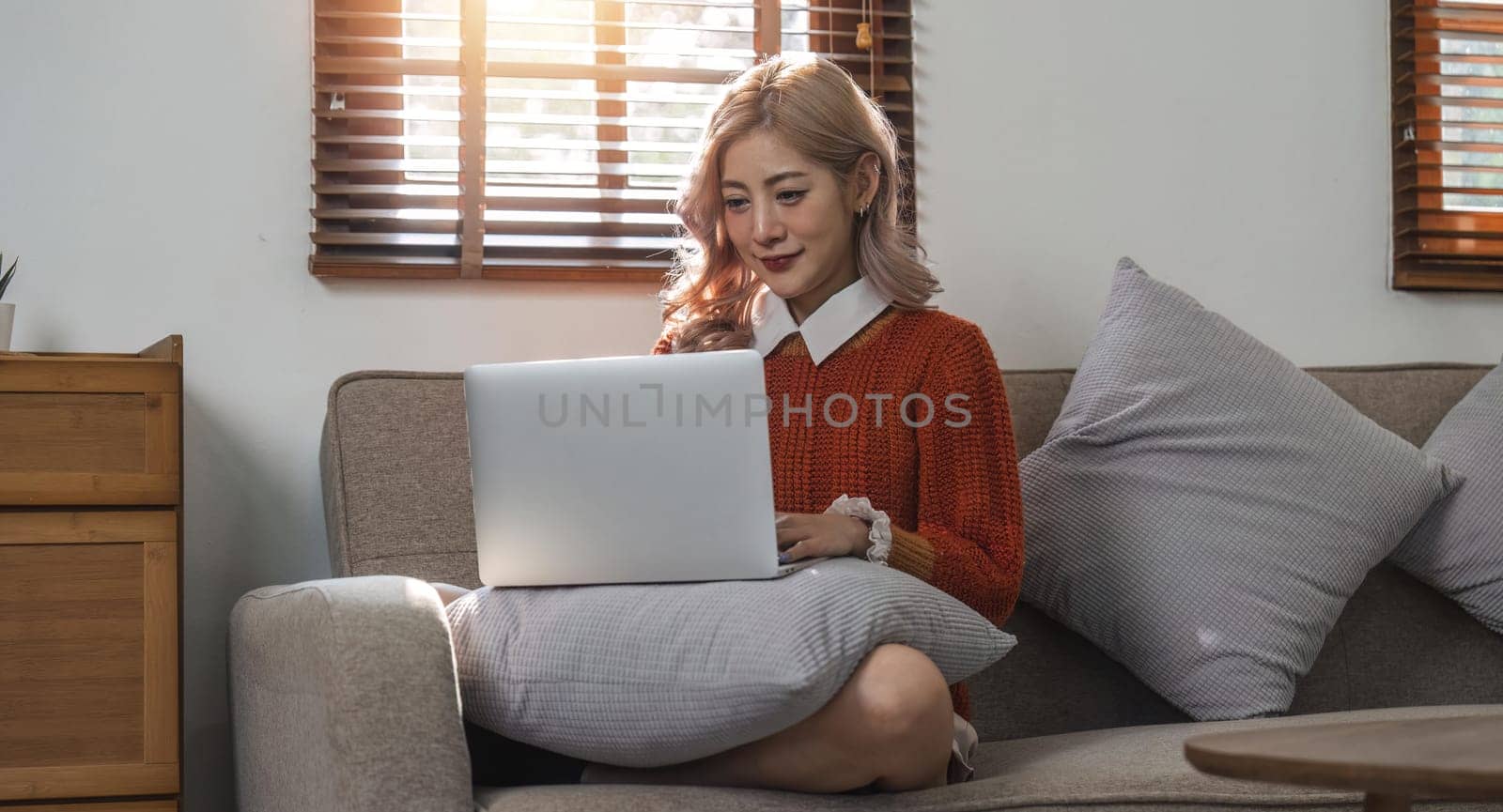 woman smiling and using laptop computer at home sitting comfortably on a sofa in living room. Smart working female people notebook. Surfing the web. Enjoying technology and connection.