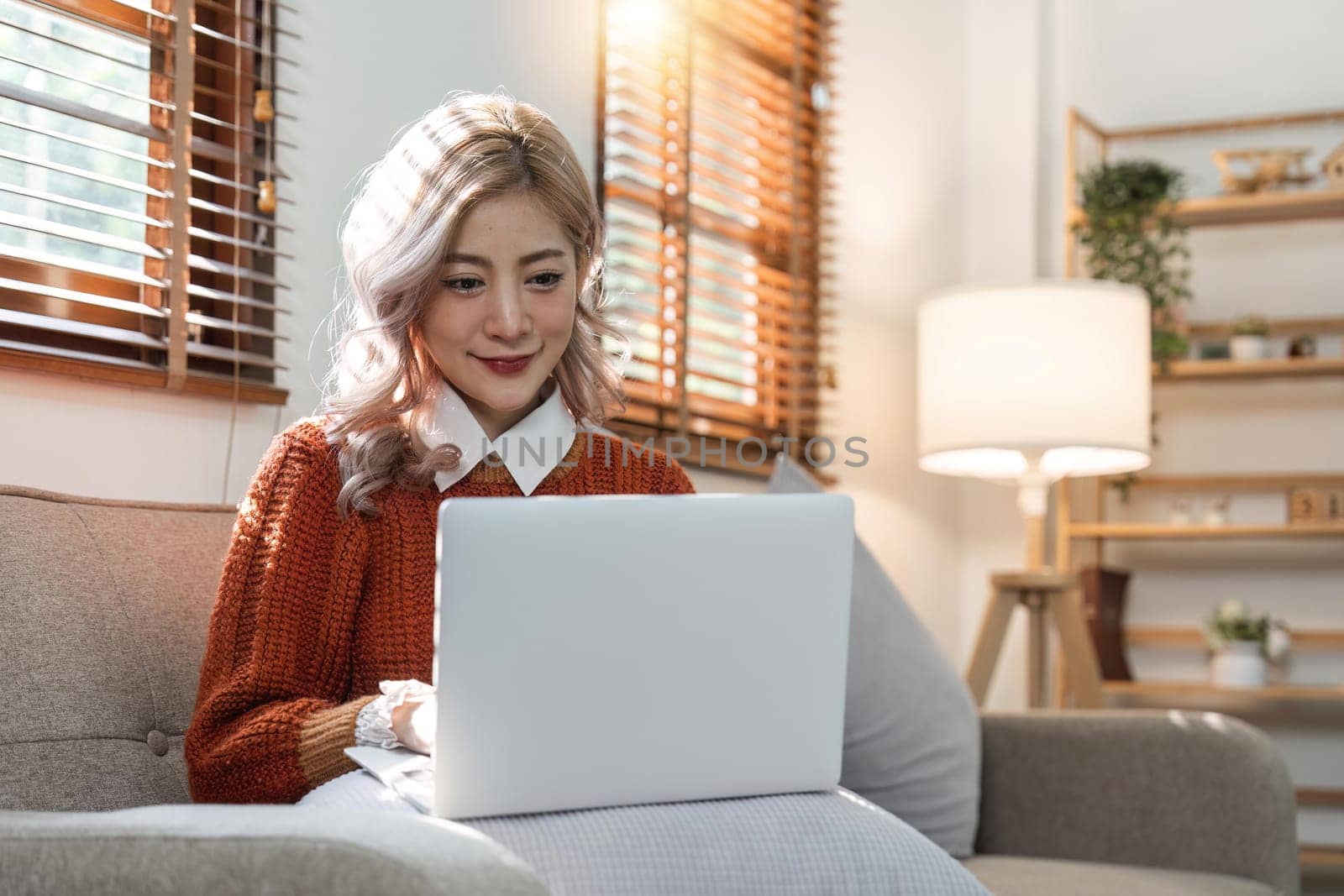 woman smiling and using laptop computer at home sitting comfortably on a sofa in living room. Smart working female people notebook. Surfing the web. Enjoying technology and connection.