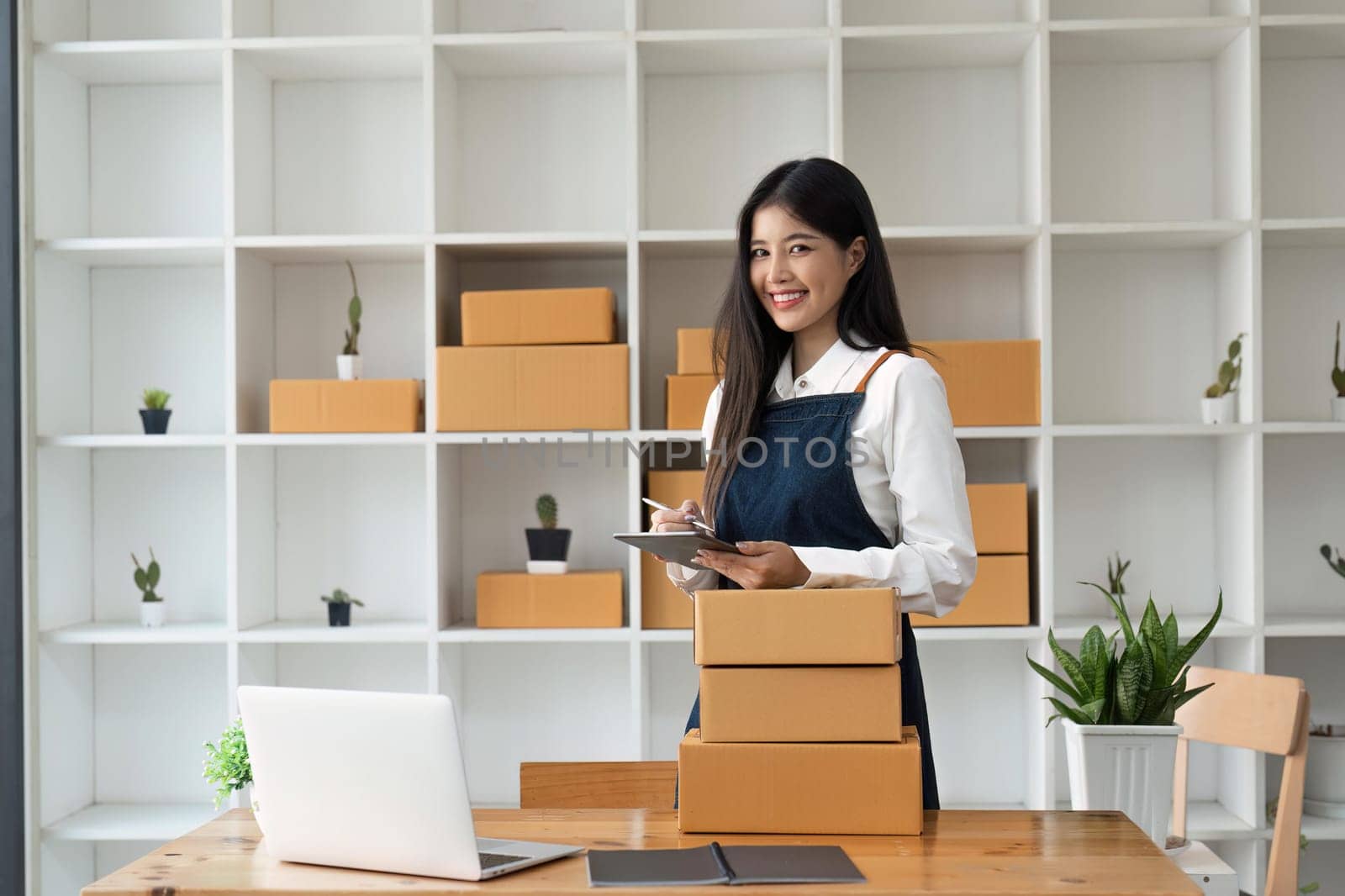 Startup SME small business entrepreneur of freelance Asian woman using tablet and box to receive and review orders online to prepare to pack sell to customers, online sme business ideas by nateemee