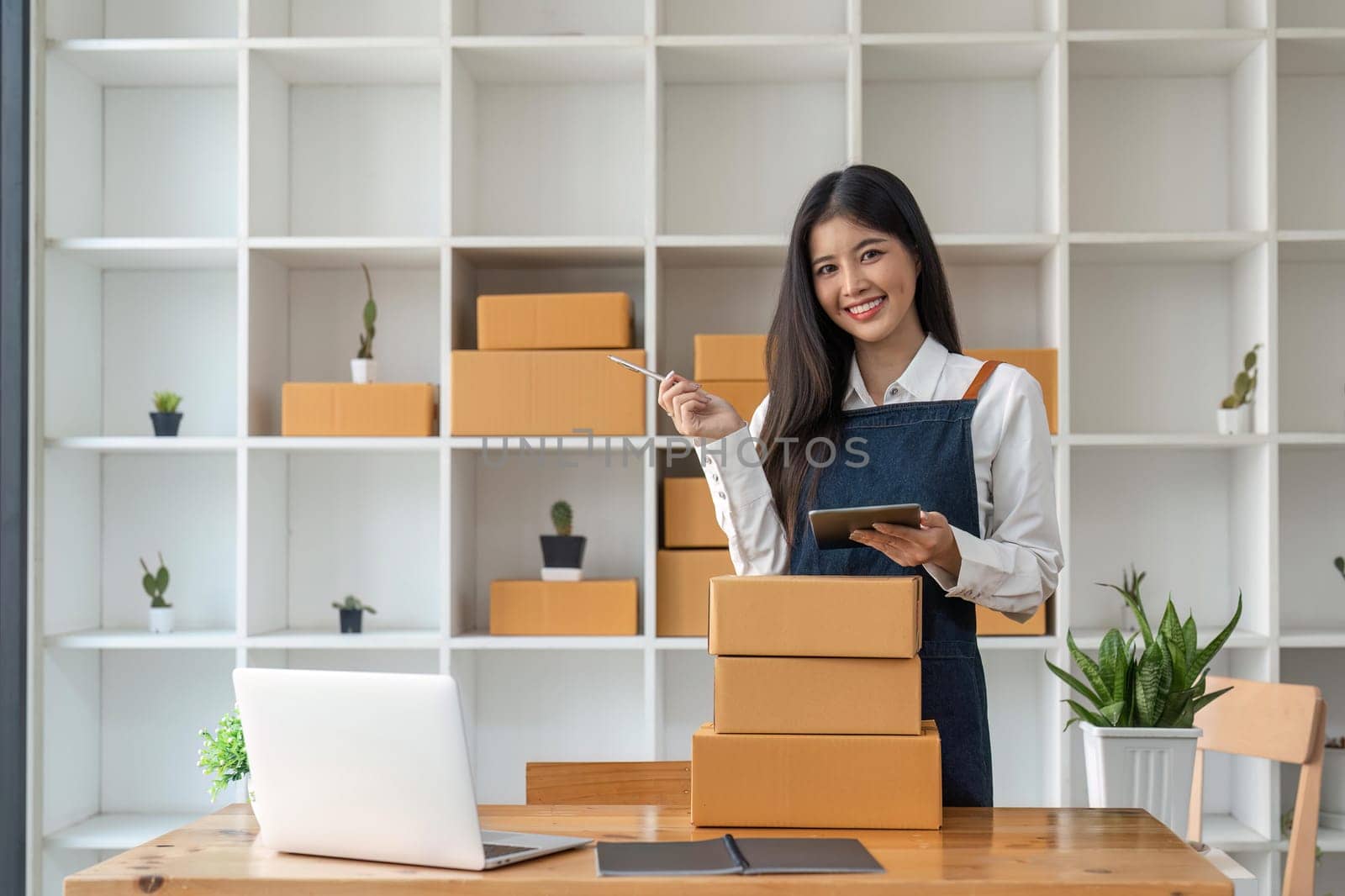 Startup SME small business entrepreneur of freelance Asian woman using tablet and box to receive and review orders online to prepare to pack sell to customers, online sme business ideas.