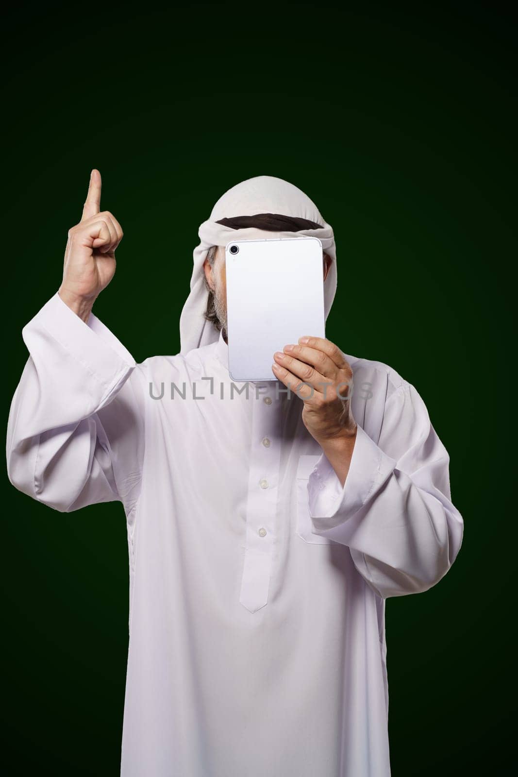 Muslim anonymous concept. Arab person holds digital tablet, face covered, index finger up, representing the concept of Islamic censorship online. Image portrays issues of privacy, security, and anonymity in the digital world. by LipikStockMedia