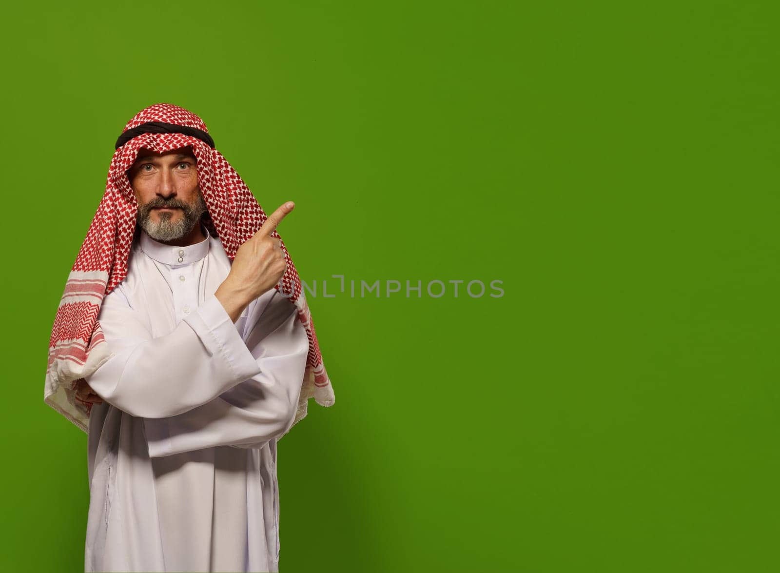 mature Muslim man in a traditional dishdasha points his finger towards copy space symbolizing concept of Sharia law, the Islamic legal system based on teachings of Quran and Hadith. authority, leadership, and principles of justice and ethics within the legal framework of Sharia law, with copy space for additional text or design elements. by LipikStockMedia