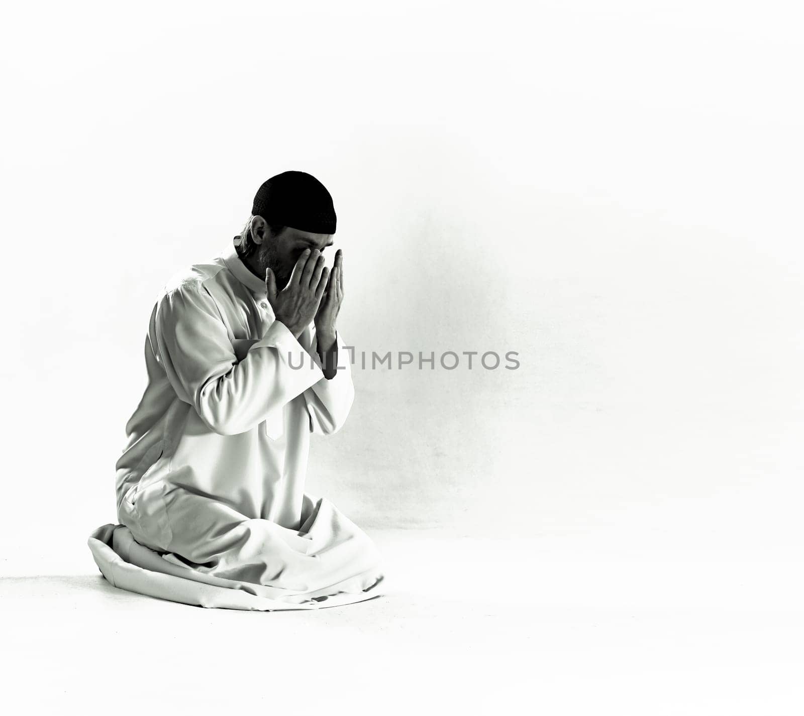 Islam religious concept.Muslim man in traditional clothing kneels on prayer mat, holds palms in front of face and performs Salah, ritual prayer of Islam. devotion, piety, and spiritual aspect of Islamic culture, with copy space for additional text or design elements. High quality photo