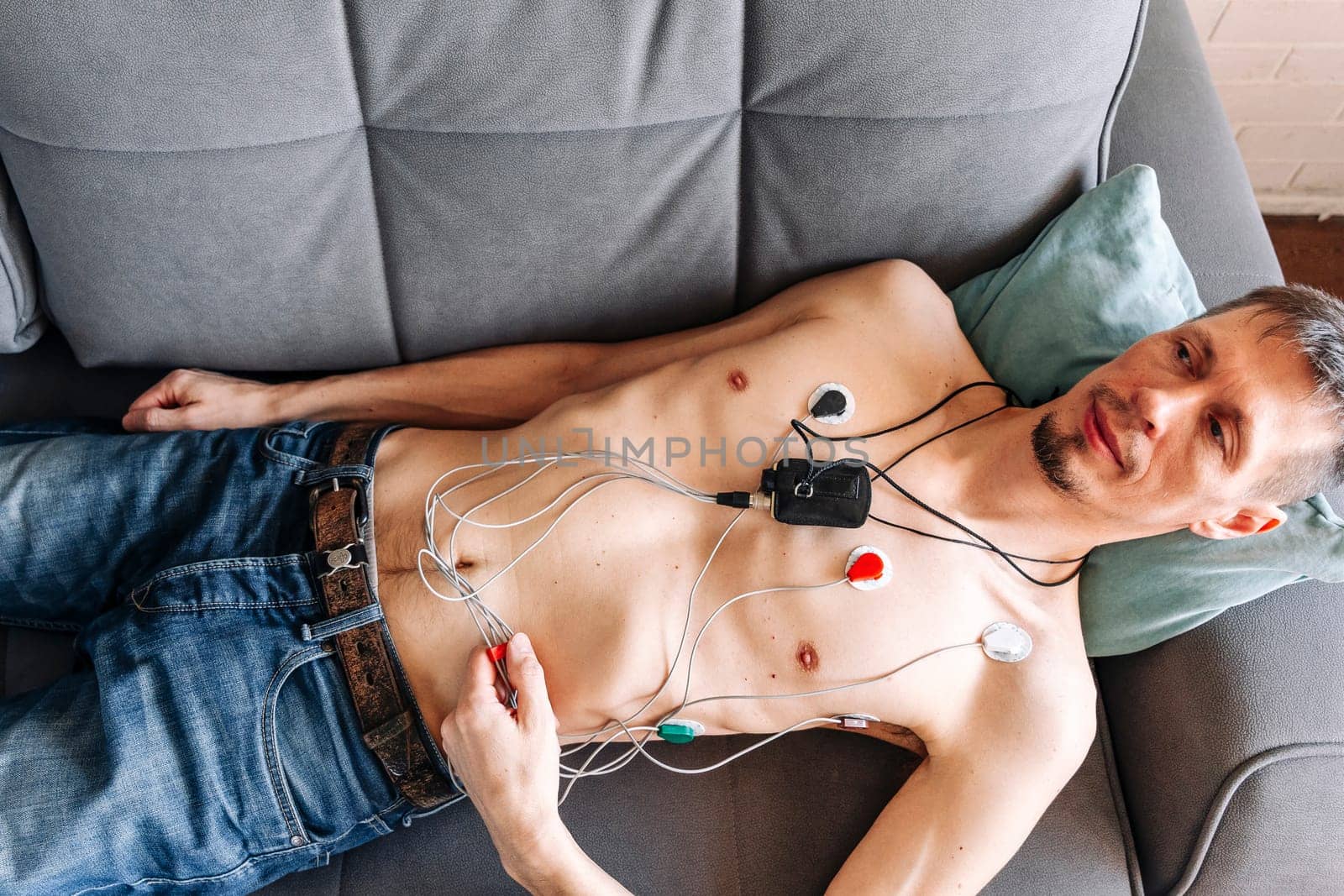 a man lying on a sofa with a Holter heart monitor connected, cardiology. Medical diagnostics. ECG sensors and wires. A man wearing portable holter monitor device. Recording cardiogram for 24 hours. Arrhythmia. diagnosis of cardiac activity. prevention, monitoring, heart problems