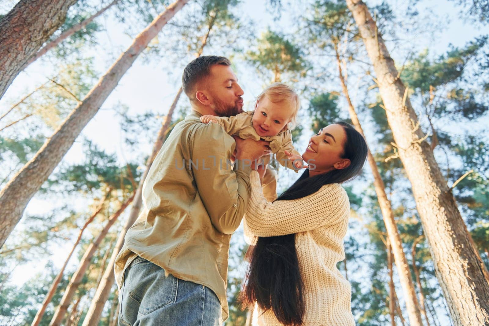 View from below. Happy family of father, mother and little daughter is in the forest by Standret