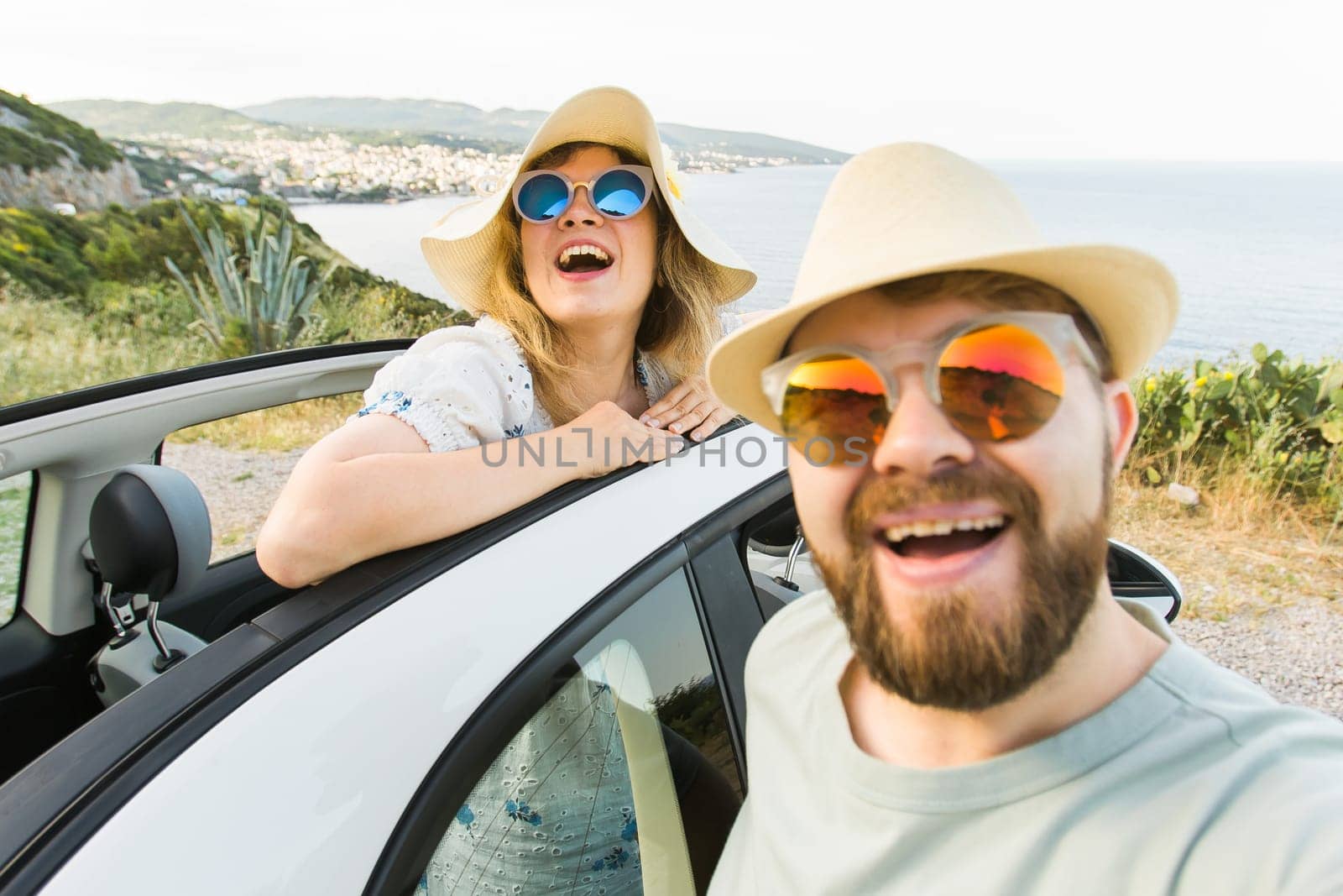 Romantic couple making selfie on smartphone camera in rental cabrio car on ocean or sea beach enjoying summer vacation together and taking picture on cellular resting near sea on weekends by Satura86