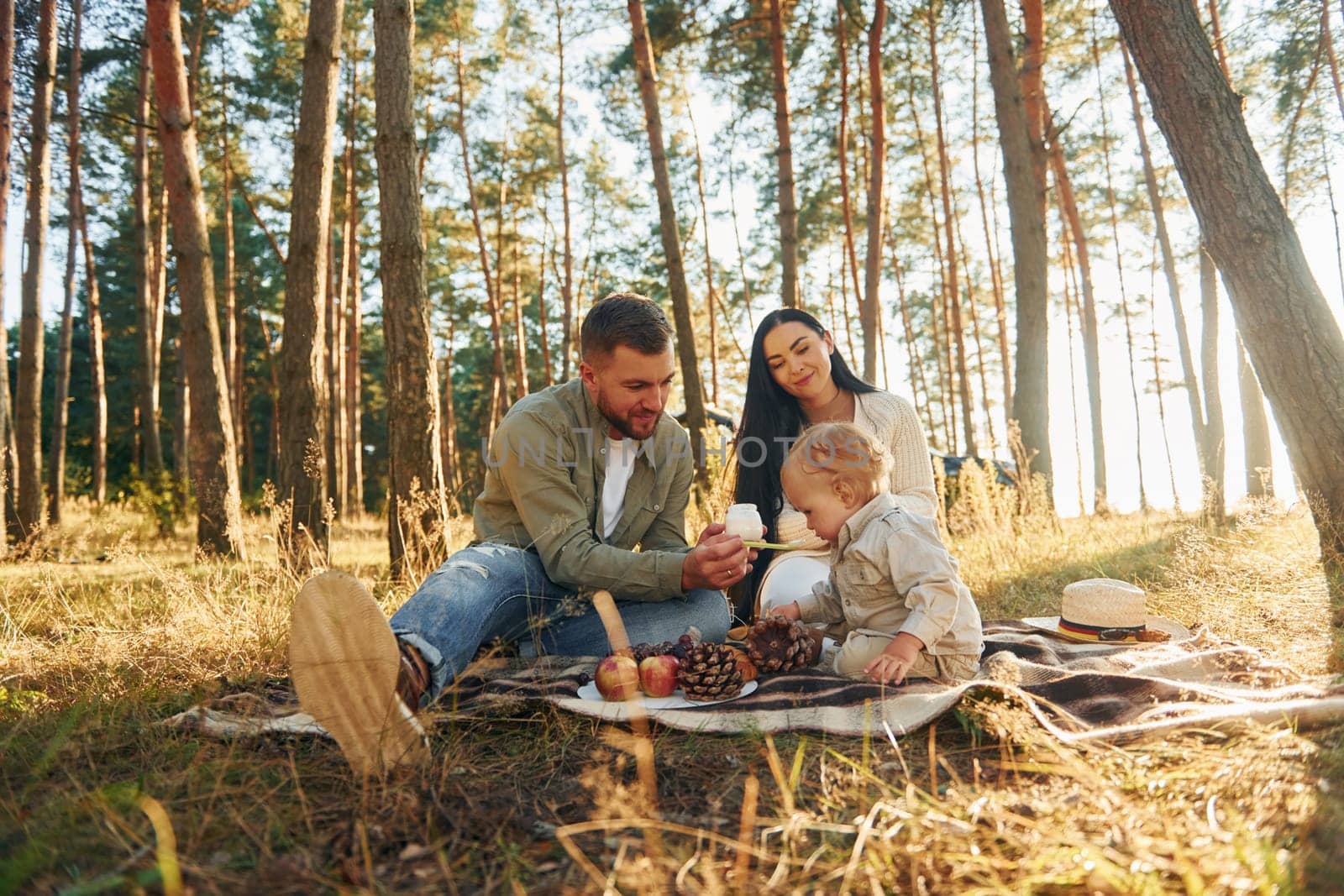 Eating some food. Happy family of father, mother and little daughter is in the forest by Standret