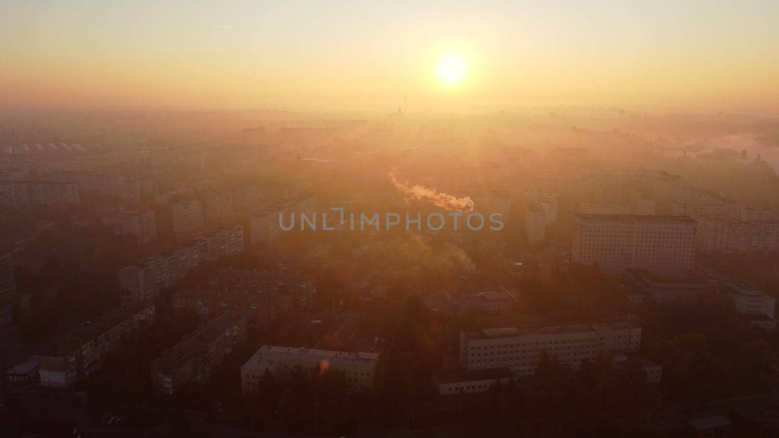 Beautiful cityscape in summer at sunrise. Flying over many multi-storey buildings and a chimney with white smoke. Bright shining sun. Urban landscape. Dawn sunrise dawning sunset sundown, rising sun.