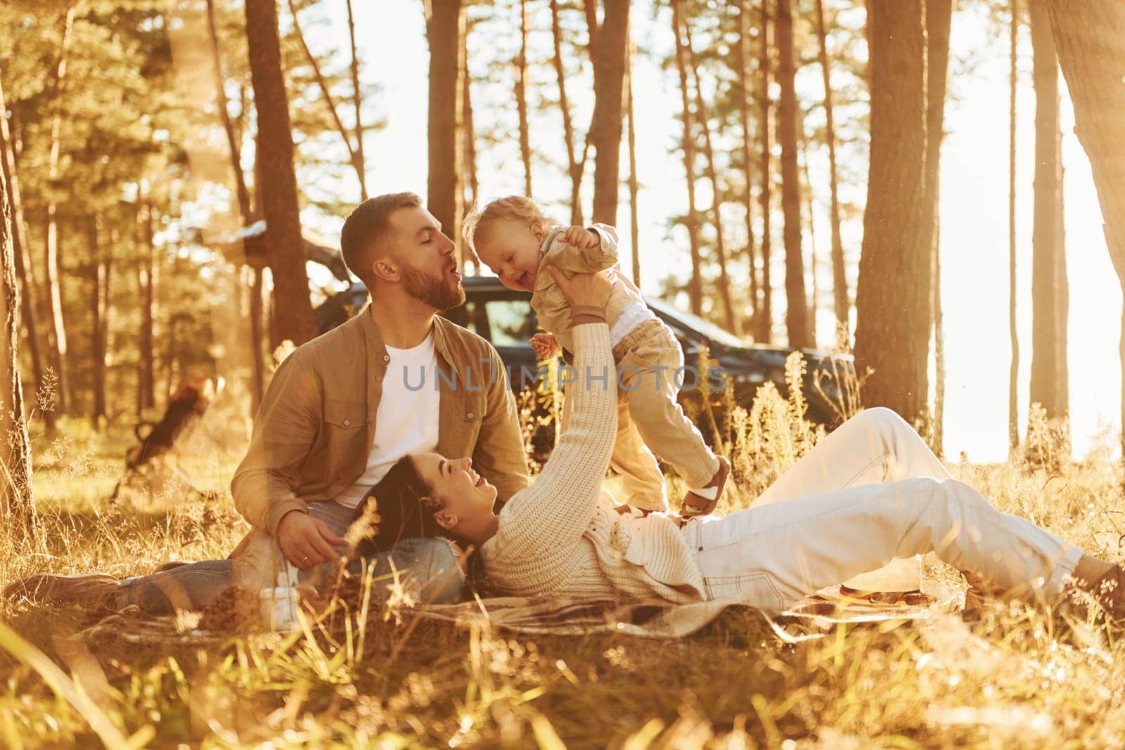 Woman is laying down. Happy family of father, mother and little daughter is in the forest by Standret